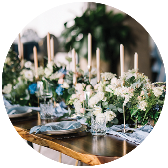 Long dinner tables covered with white cloth, served with porcelain and blue glasses and rich decorated with flowers 
