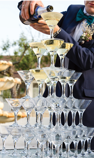 Groom filling a pyramid of glasses with champagne at outdoor garden in wedding ceremony