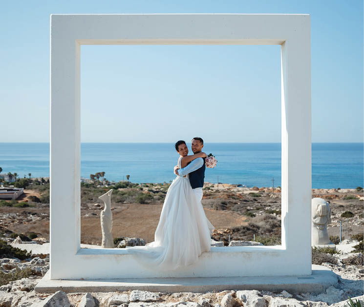 Beautiful smiling young bride and groom walking on the beach, kissing and having fun, wedding ceremony near the rocks and sea. Wedding ceremony on coast of Cyprus
