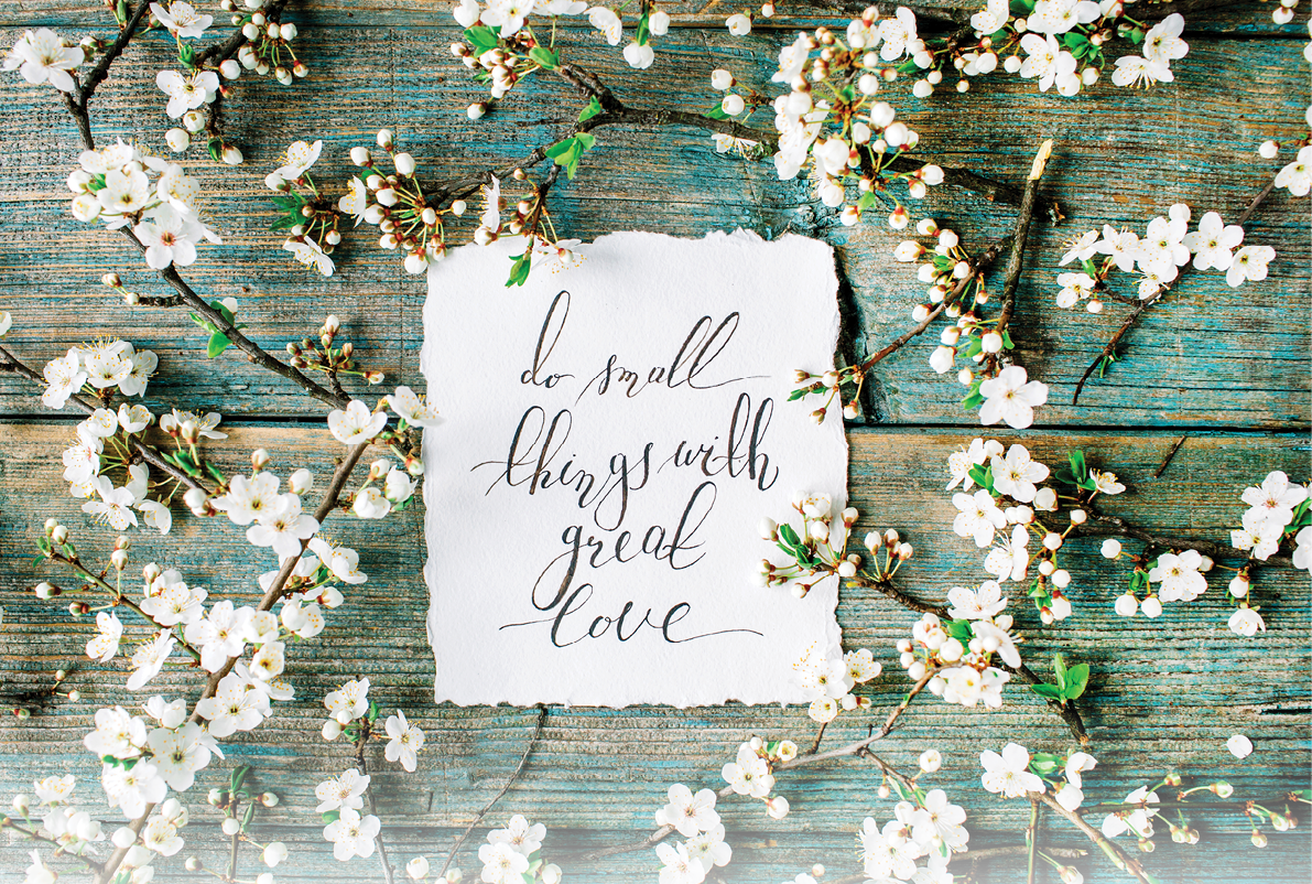 inspirational quote “Do small things with great love" written in calligraphy style on paper with wreath frame of flowers isolated on old wooden mint table background. flat lay, overhead view, top view