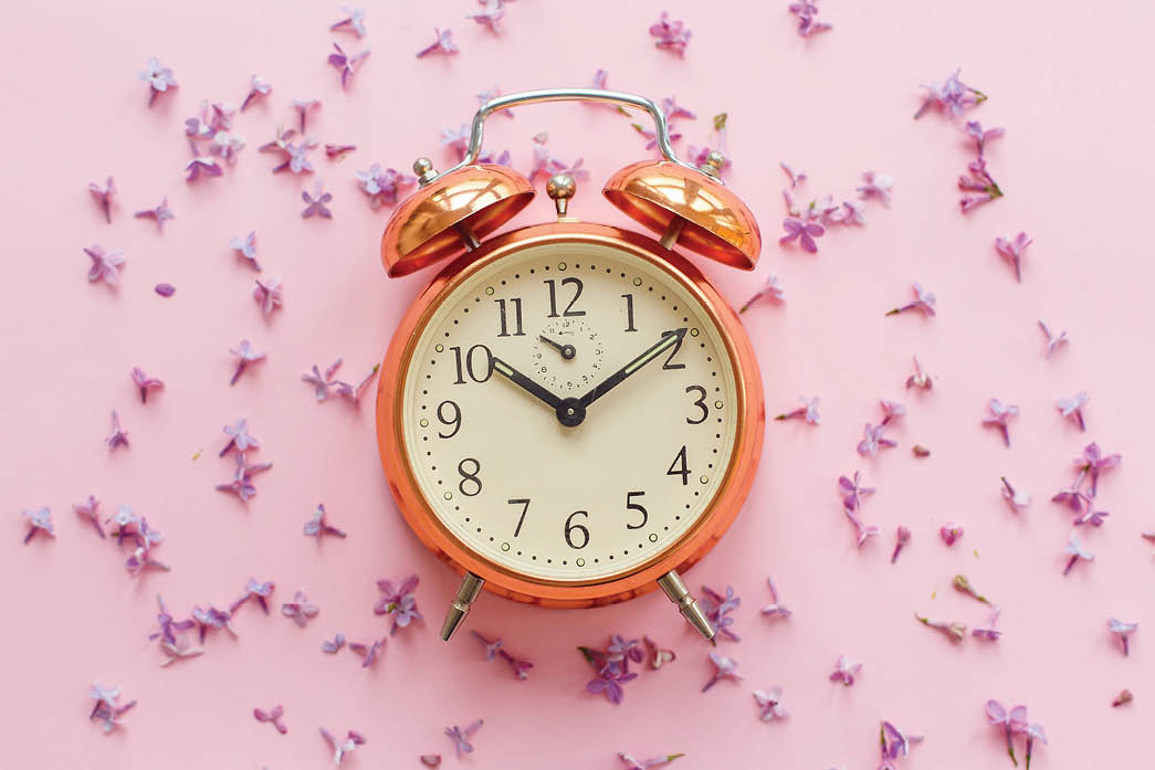 stylish vintage alarm clock on pink background with lilac flowers. creative flat lay with space for text. time concept. modern fashion image. summer vacation concept. time to travel