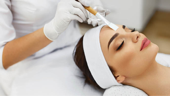 Face Skin Care  Beautician Applying Beauty Oil Mask On Face Using Brush In Spa Salon  Closeup Of Female Client Getting Hydrating Procedure In Beauty Clinic  Cosmetology  High Resolution