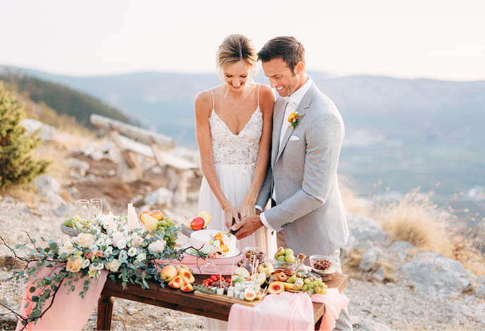 The bride and groom are cutting a cake during a buffet table after the wedding ceremony on Mount Lovcen and smiling
