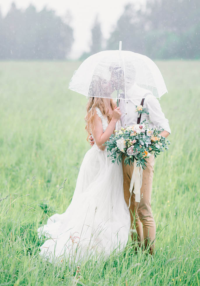 The bride and groom hid from the rain by an umbrella  The bride and groom kissing under an umbrella 