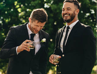 Groom and best man drinking and smiling during wedding party. Groom and groomsmen partying after wedding.