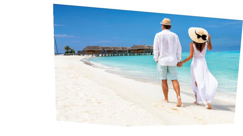 Happy couple in white clothing and with hats walks down a tropical beach with turquoise sea in the Maldives islands