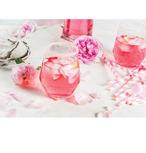 Summer refreshment drinks  Light pink rose cocktail, with rose wine, tea rose petals, lemon  On a white stone concrete table  With striped pink tubules, petals and rose flowers  Copy space