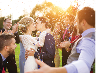 Full length portrait of newlywed couple and their friends at the wedding party showered with confetti in green sunny park