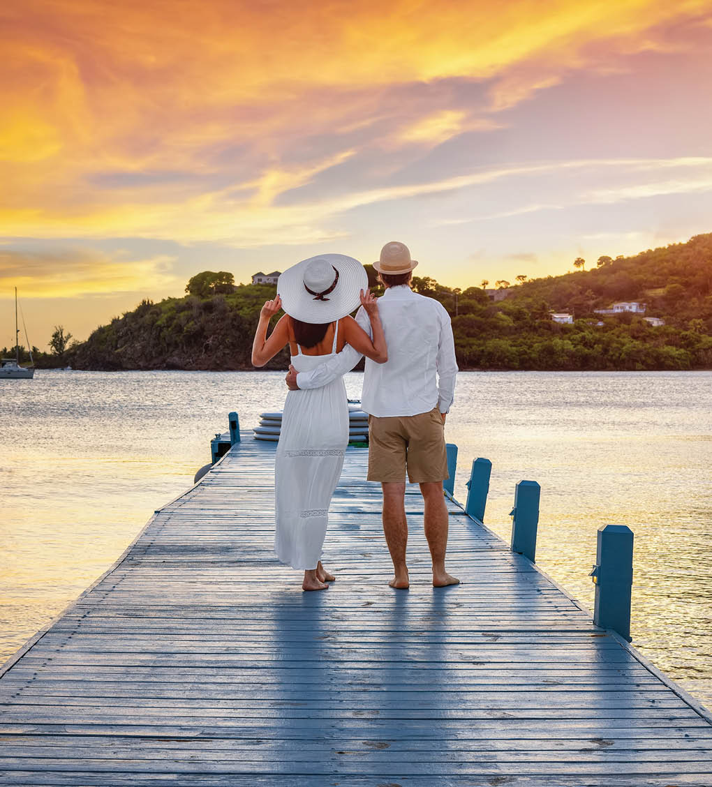 A beautiful honemyoon couple on a pier enjoys the tropical sunset in the Caribbean Sea, Antigua and Barbuda island