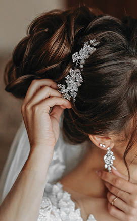The hairdresser makes a fashionable and stylish styling on the bride's hair. Beautifies a hairdress with a beautiful precious accessory made of white beads